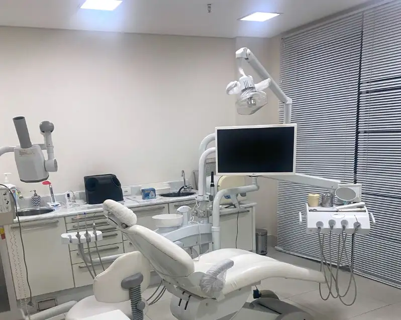 A sala de atendimento do consultório: cadeira odontológica branca, monitor e persianas